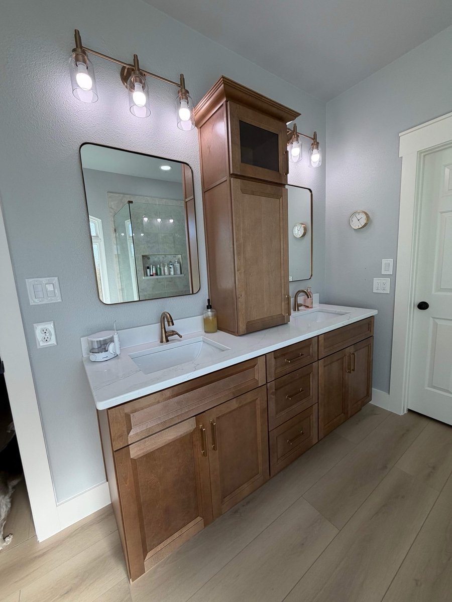 Wood double vanity with center storage tower, framed mirrors, and gold faucets