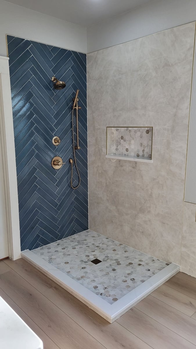 Walk-in shower with blue herringbone wall, gold fixtures, and hexagon mosaic floor