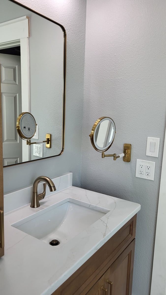 Quartz vanity with gold faucet, framed mirror, and round gold magnifying mirror