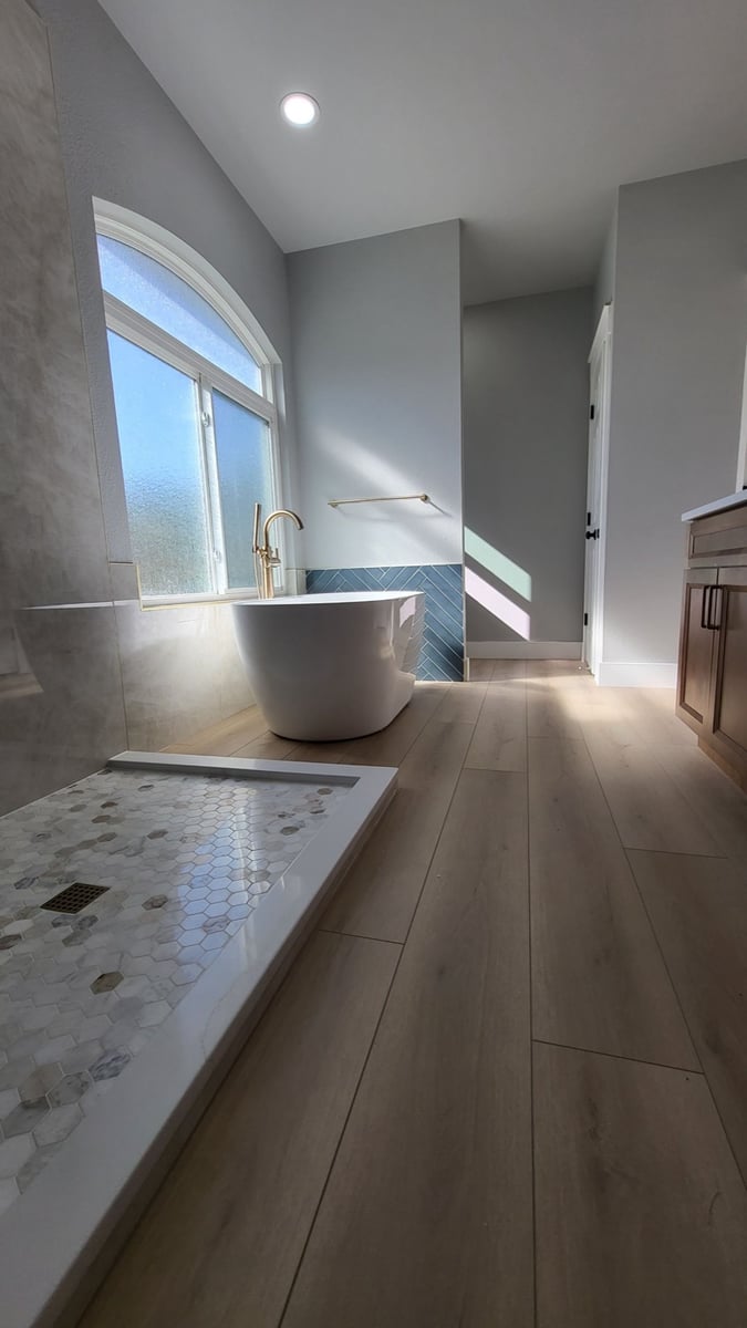 Long master bath with freestanding tub, glass shower, and wood-look plank floor