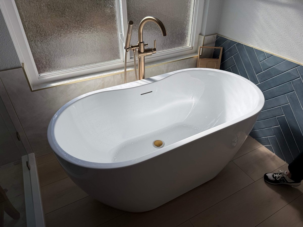 Overhead view of white freestanding tub with gold faucet by frosted window
