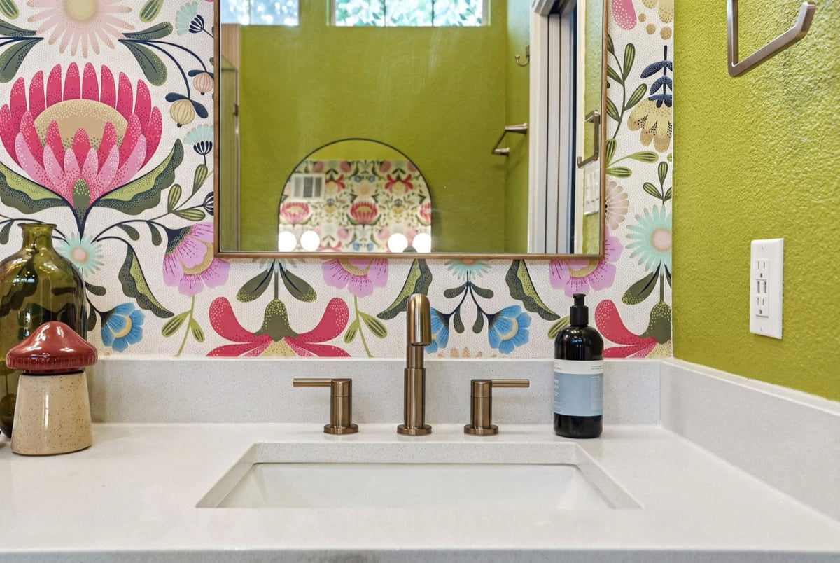 Single vanity sink with brass faucet, floral wallpaper, and green accent wall