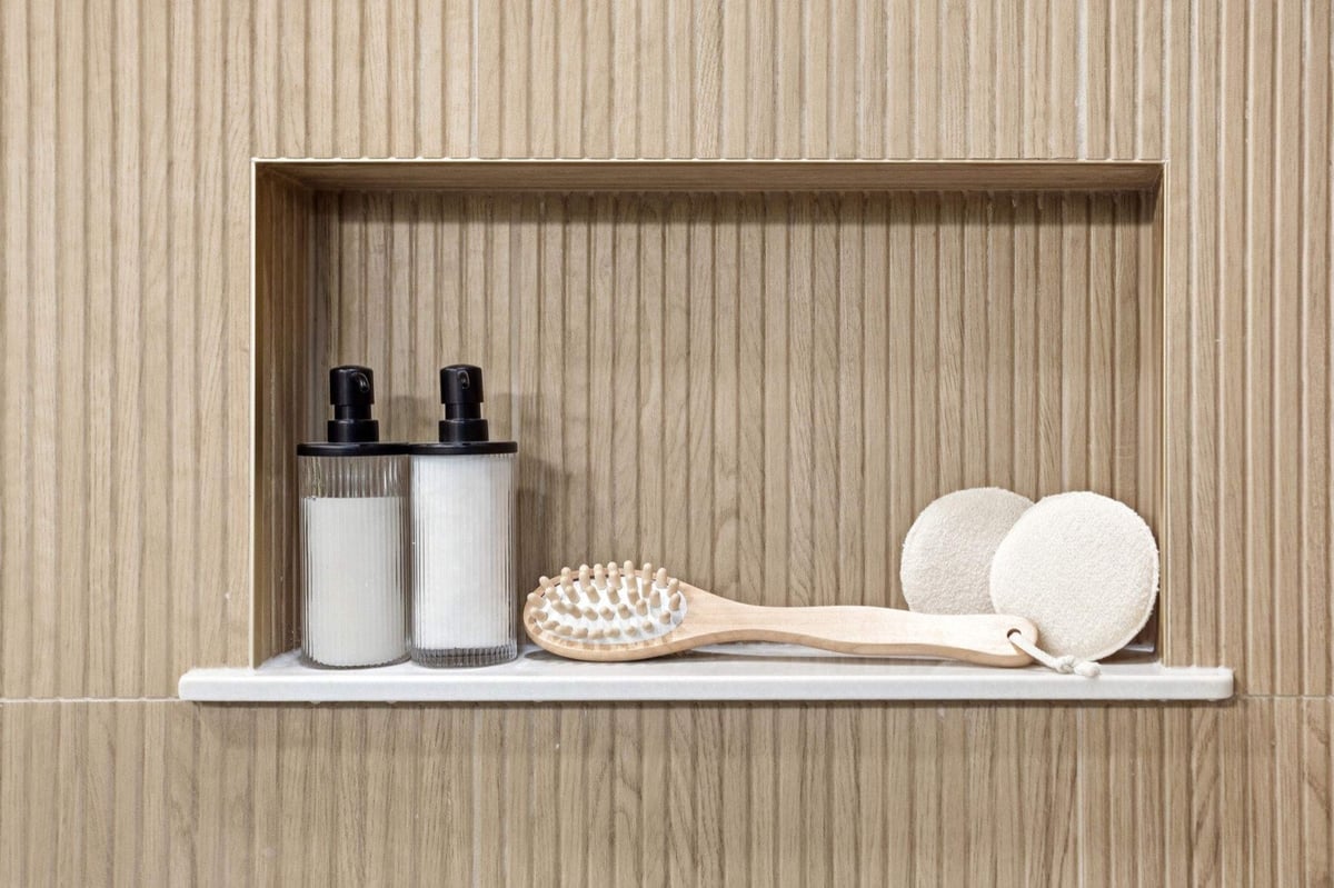 Fluted wood-look tile shower niche holding toiletries and a bath brush