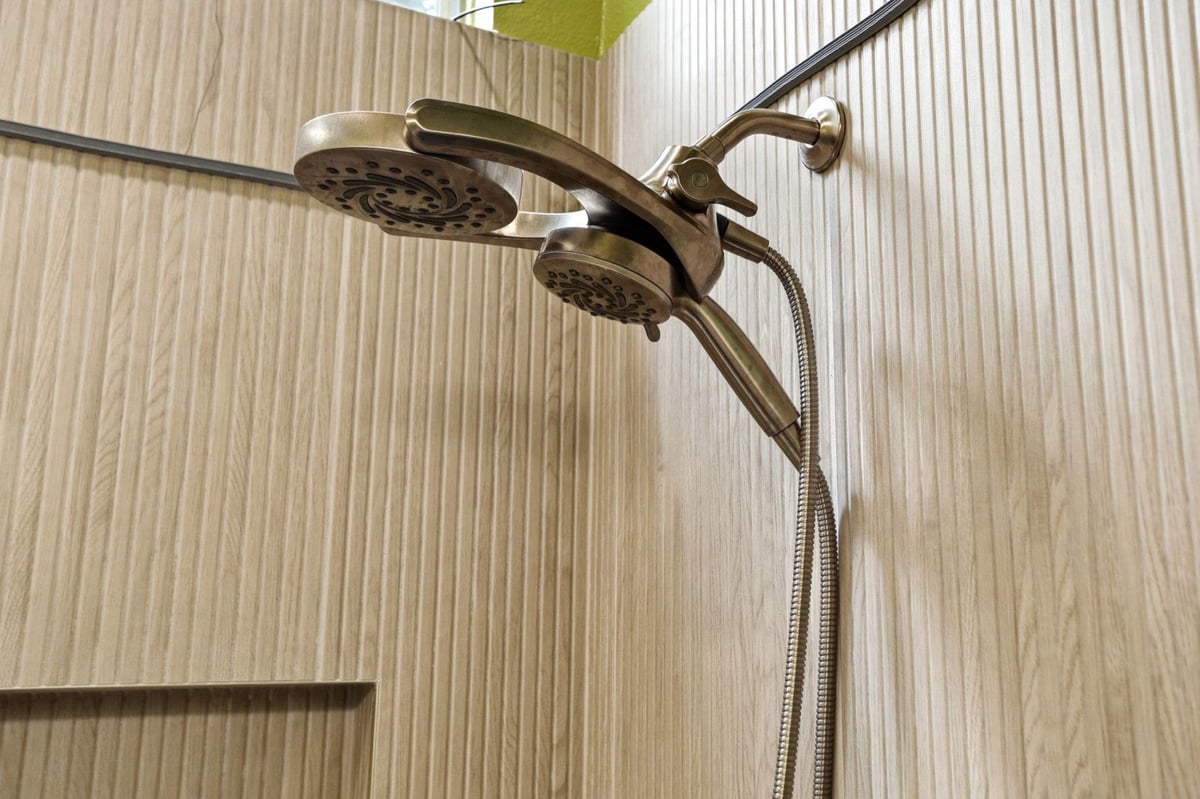 Brass dual shower head mounted on vertical fluted wood-look tile wall