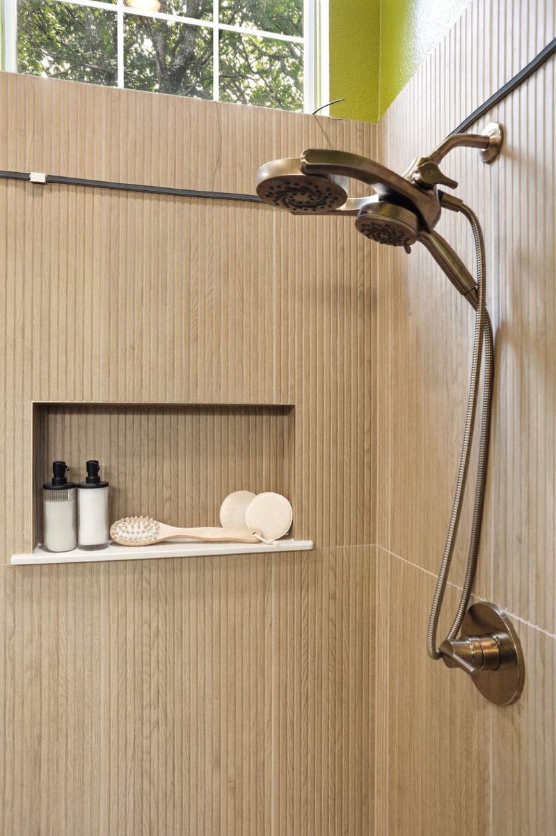 Wood-look tile shower with brass fixtures and a recessed toiletry niche