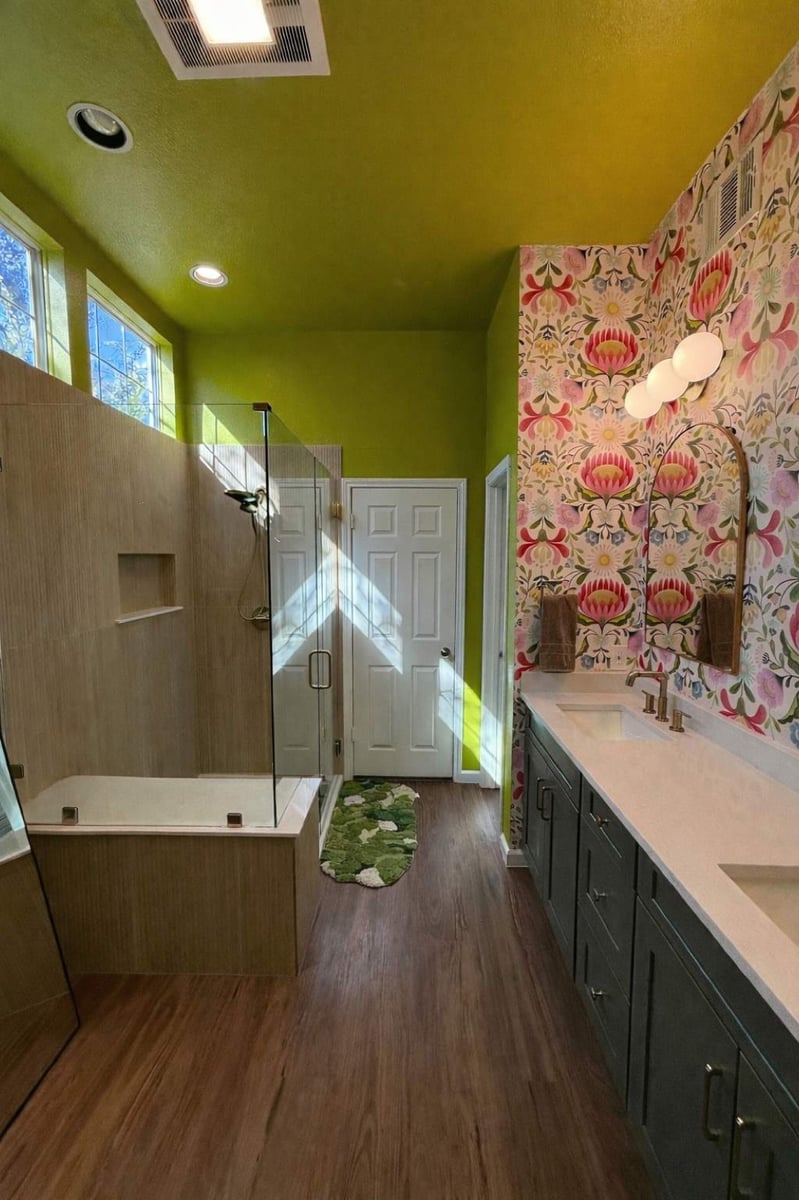 Colorful bath with green walls, glass shower, and floral wallpaper vanity wall