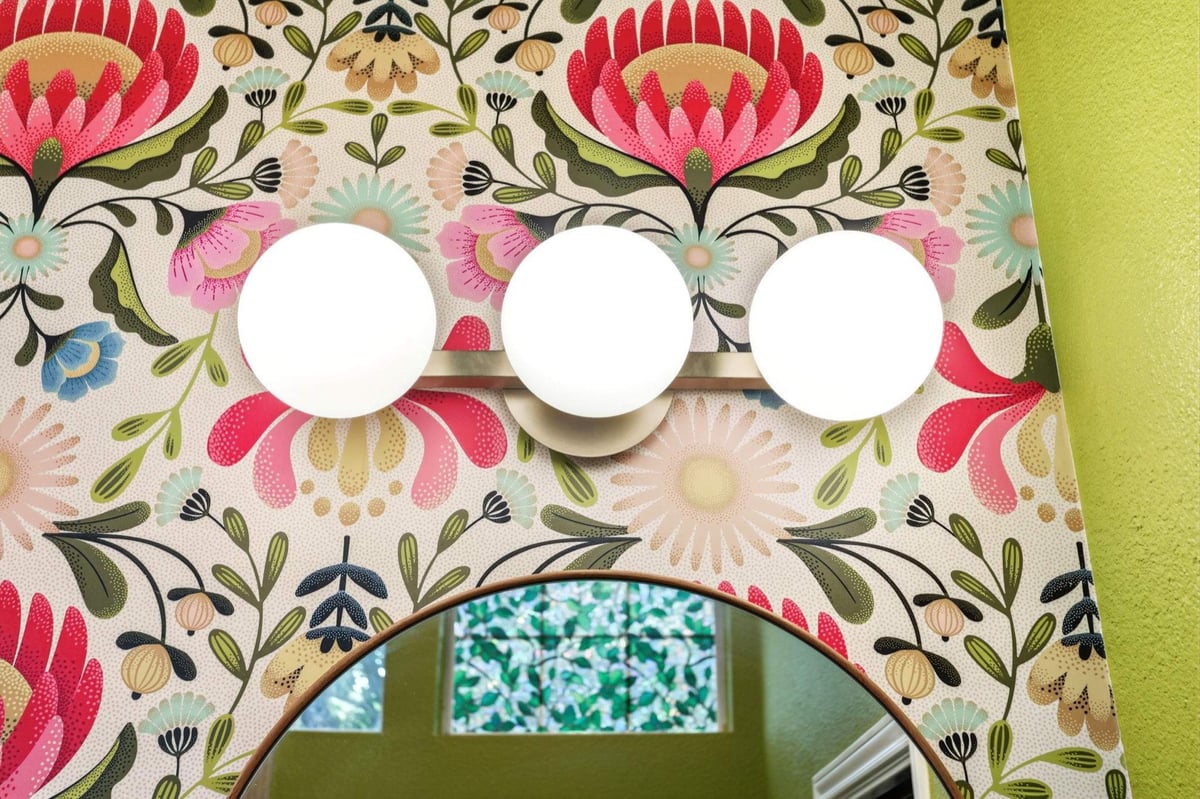 Three-globe brass vanity light mounted on bright botanical floral wallpaper