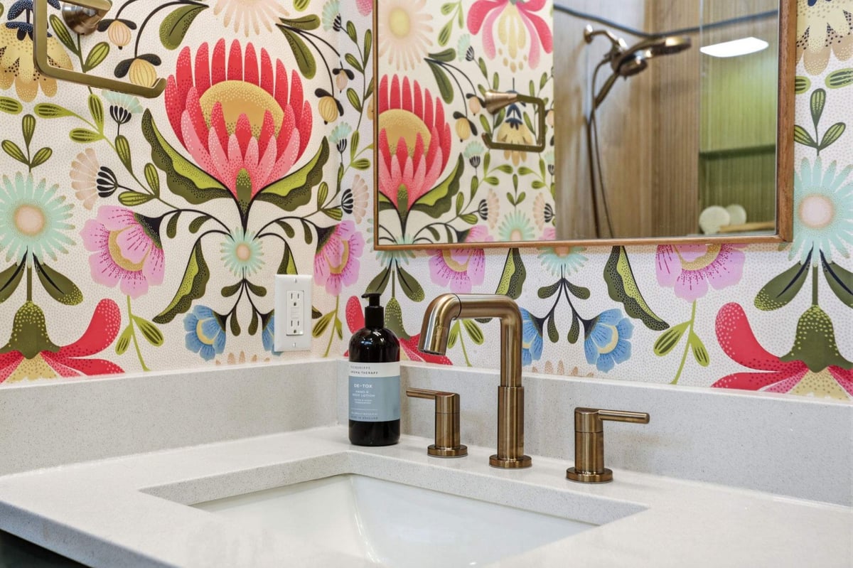 Brass faucet and white quartz sink against vibrant floral protea wallpaper