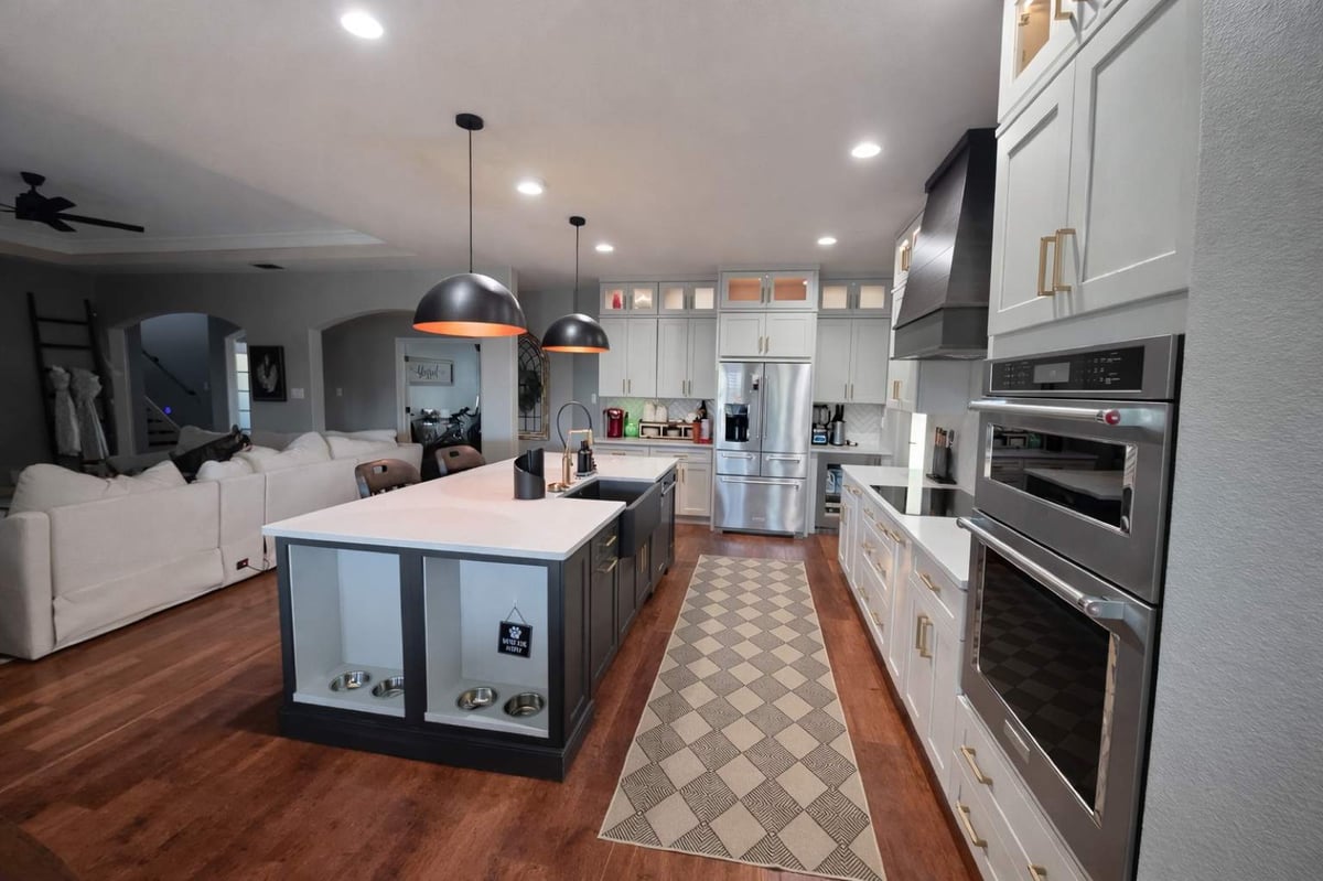 Open-concept kitchen with white island, black pendants and herringbone backsplash off living room