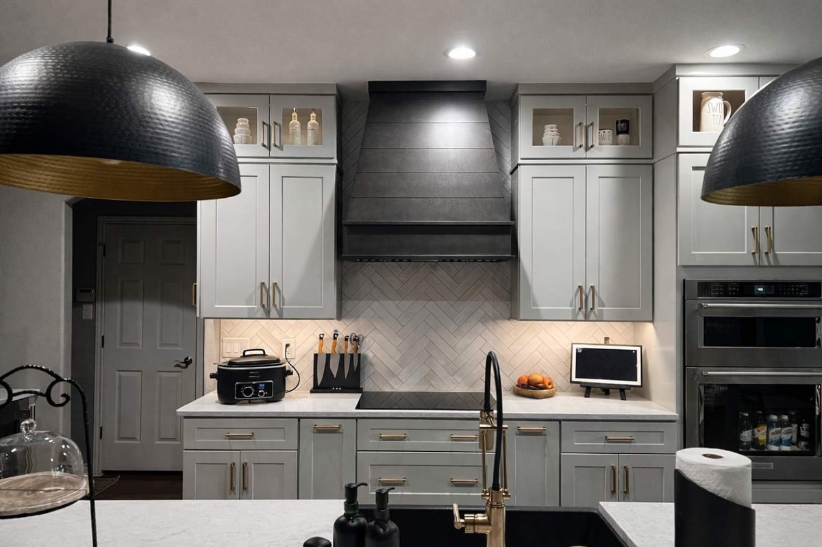 Gray cabinets with black wood vent hood, herringbone backsplash and induction cooktop