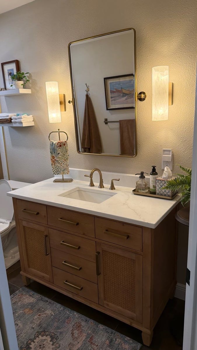 Wood vanity with white quartz top, gold faucet and arched gold-framed mirror