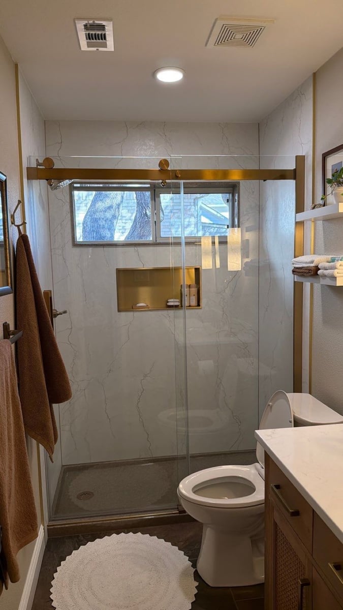 Walk-in shower with marble walls, gold sliding glass door and built-in niche