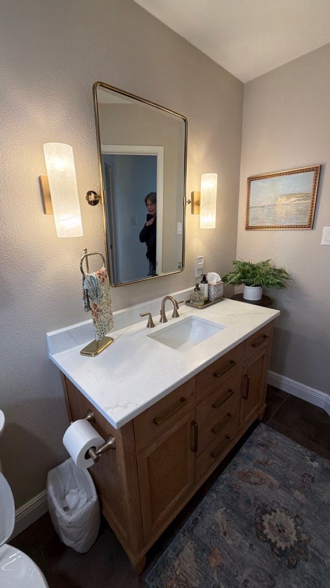 Wood vanity, quartz counter and gold mirror flanked by alabaster sconces