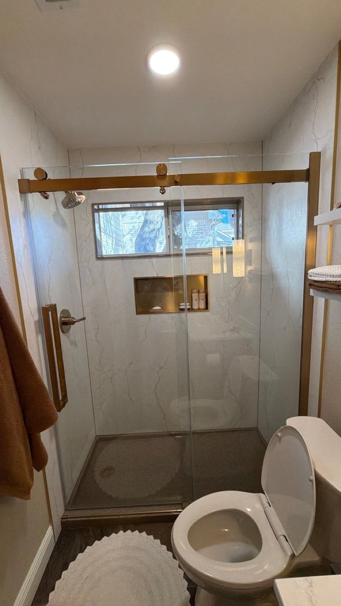 Marble-tiled shower with gold-framed sliding glass door beside white toilet