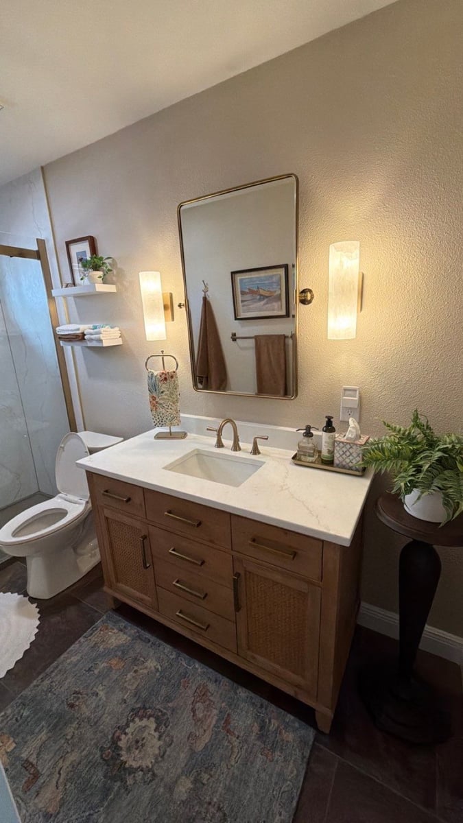 Wide view of remodeled bathroom with glass shower, wood vanity and area rug