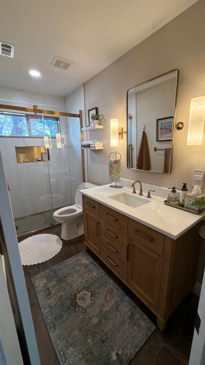 Full bathroom showing marble shower, toilet and wood vanity with gold hardware