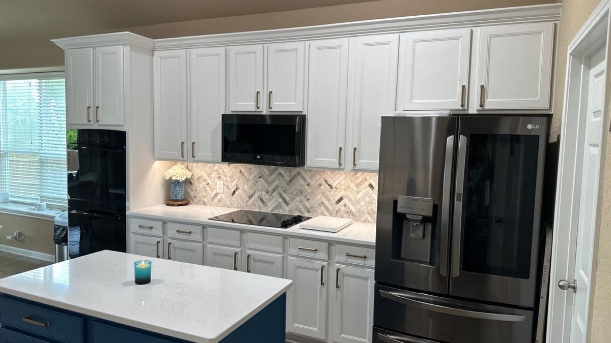 White kitchen with herringbone backsplash, black ovens, and stainless refrigerator