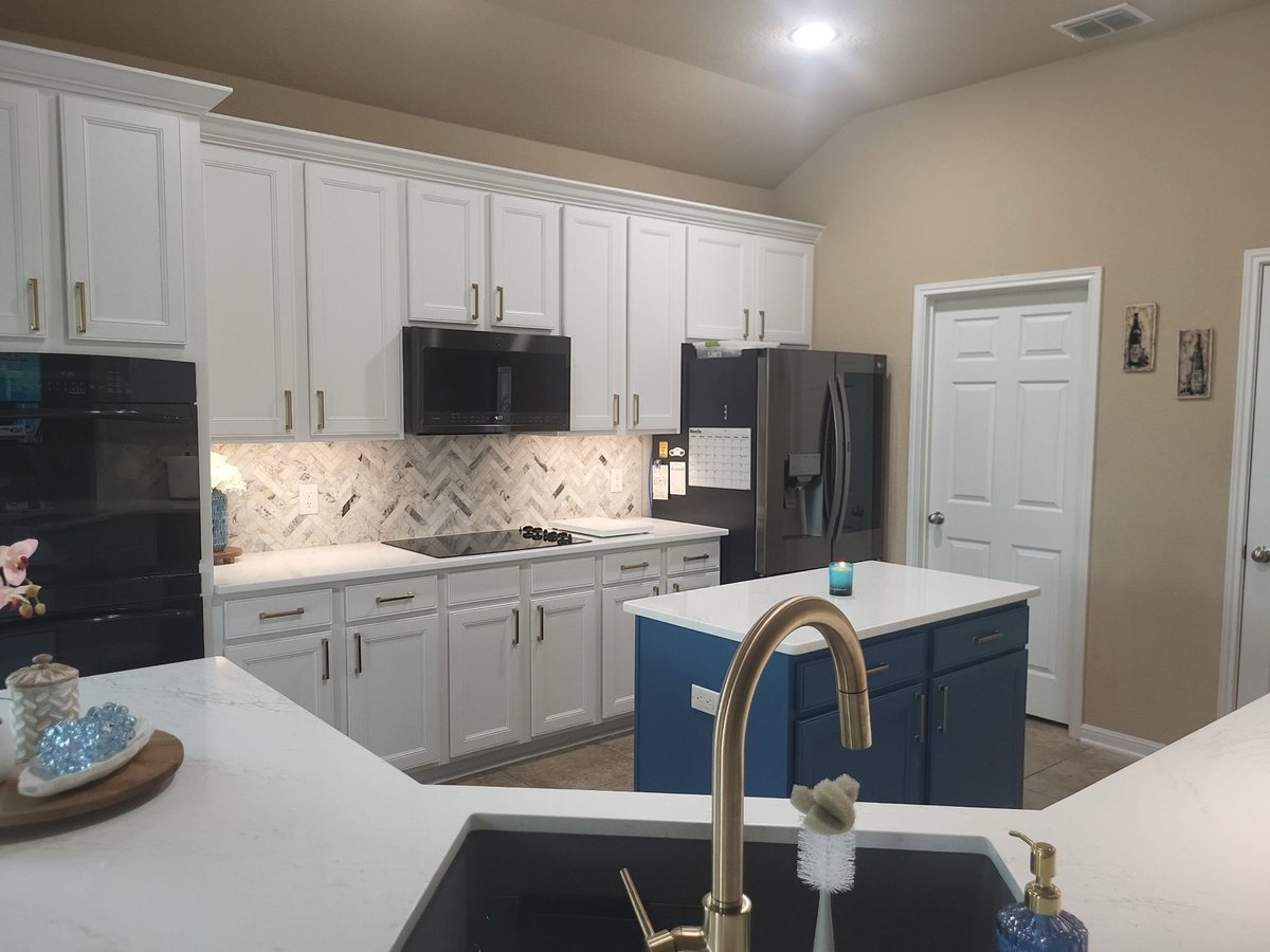 White kitchen with navy blue island, brass faucet, and herringbone tile backsplash