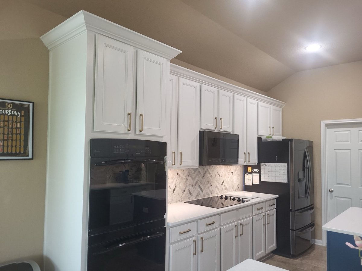White cabinets with brass pulls, black double oven, and herringbone backsplash