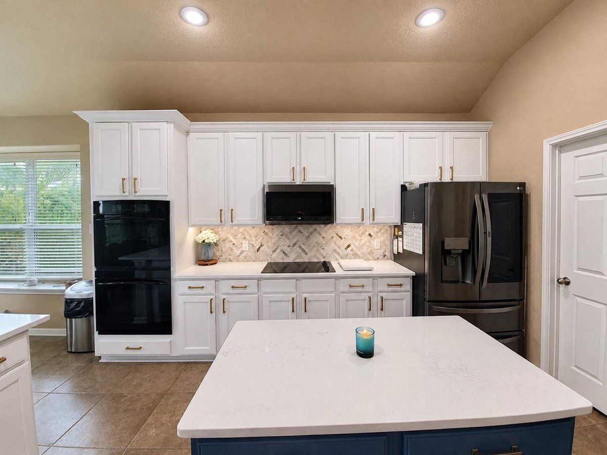 White kitchen with navy island, black appliances, and herringbone backsplash