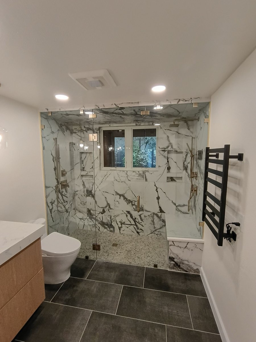 Walk-in shower with bold marble walls, glass door, and pebble floor beside floating vanity