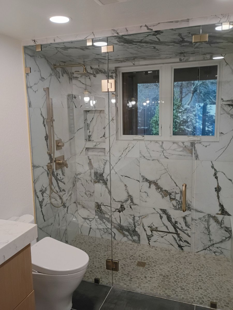 Glass shower with marble walls, brass fixtures, and a window framed by veined stone