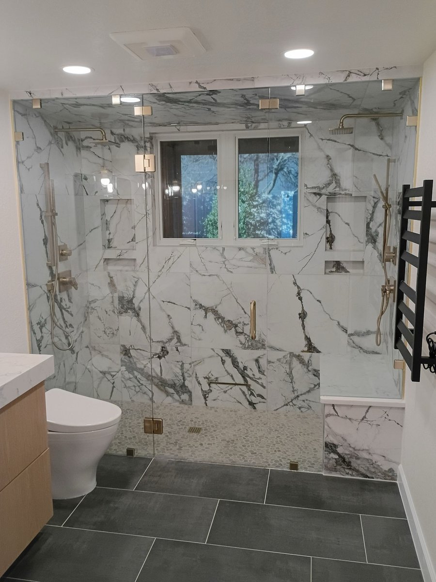 Marble walk-in shower with dual gold shower heads and dark tile floor