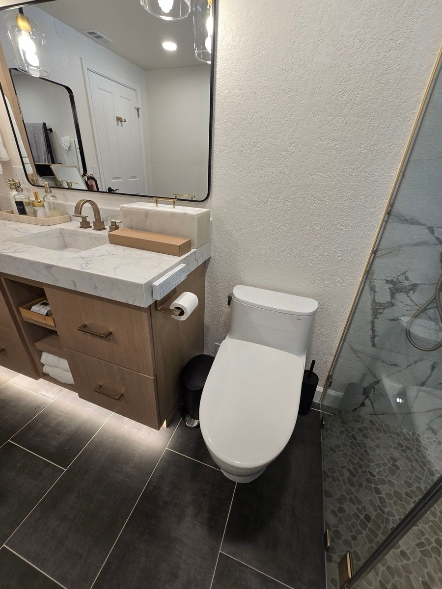 Wood vanity with marble waterfall counter, brass faucet, and frameless mirror