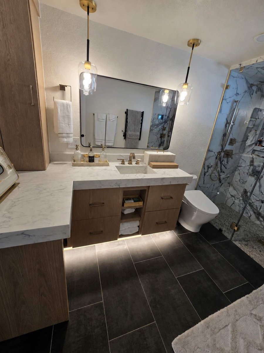 Finished master bath with wood vanity, brass pendants, and glass marble shower