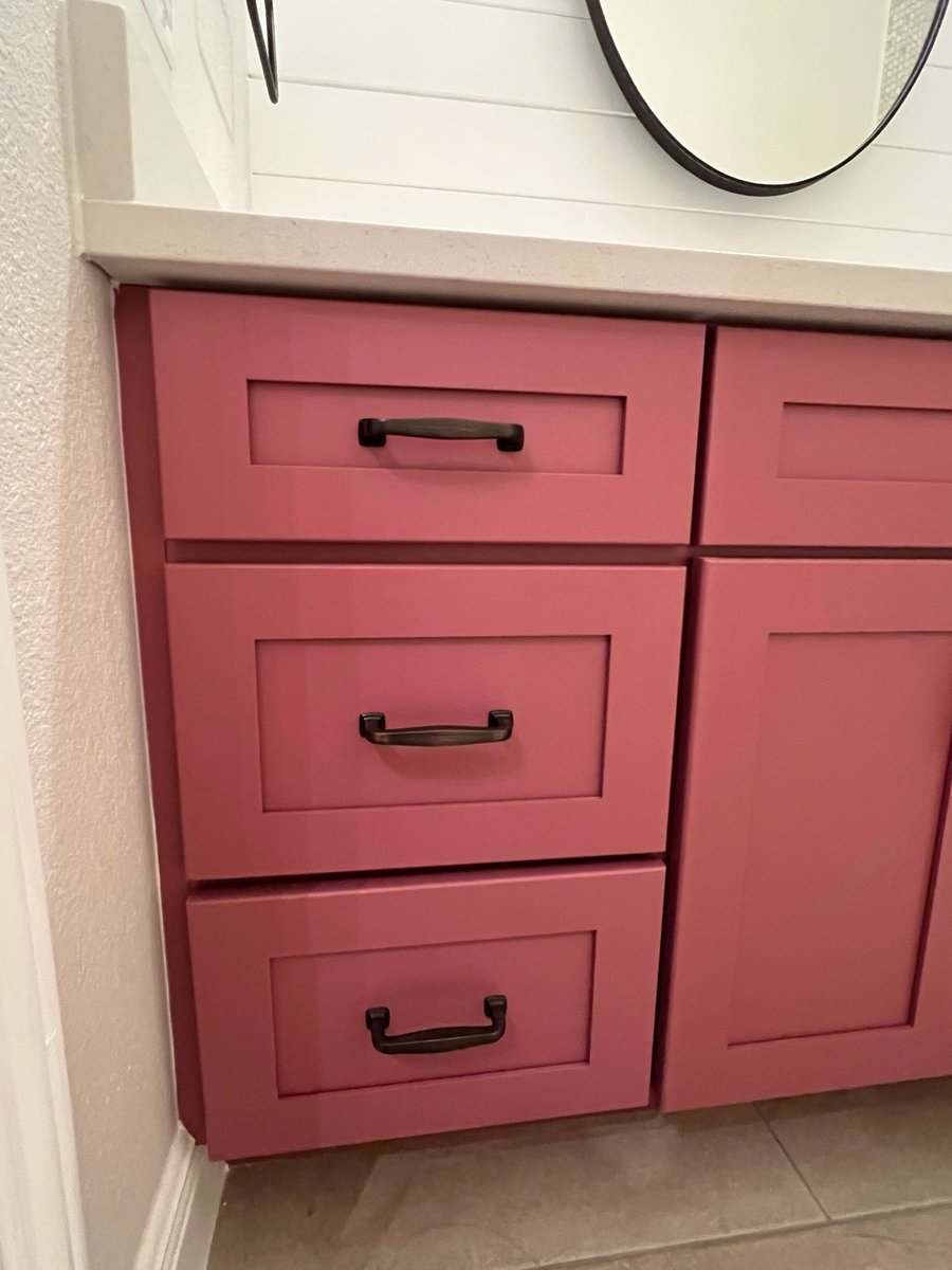 Dusty rose vanity drawers with oil-rubbed bronze pulls under round mirror