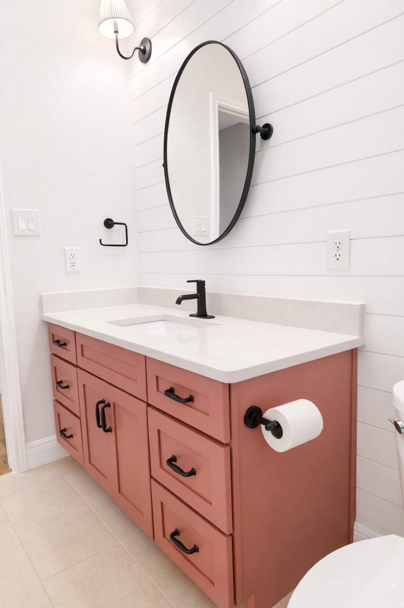 Pink-painted vanity with black faucet and oval mirror on white shiplap wall