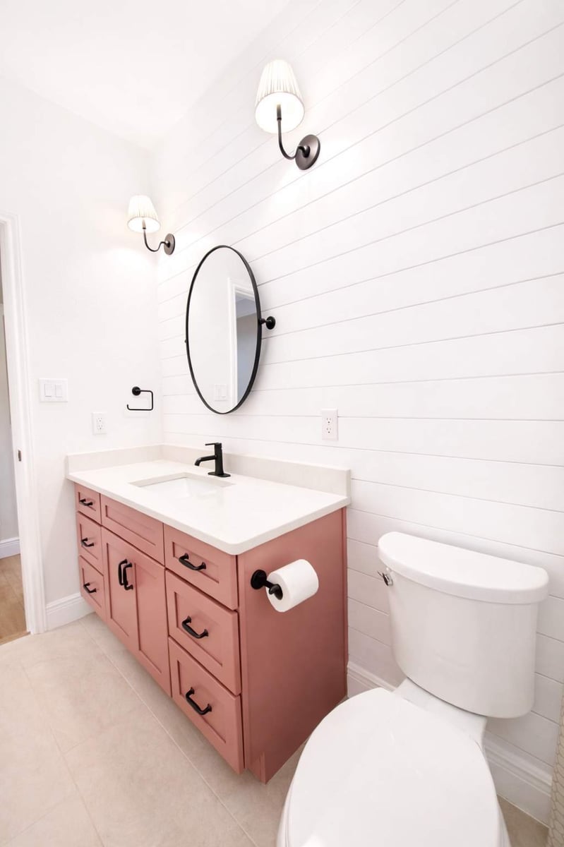 Mauve vanity and white shiplap wall with sconces beside white toilet