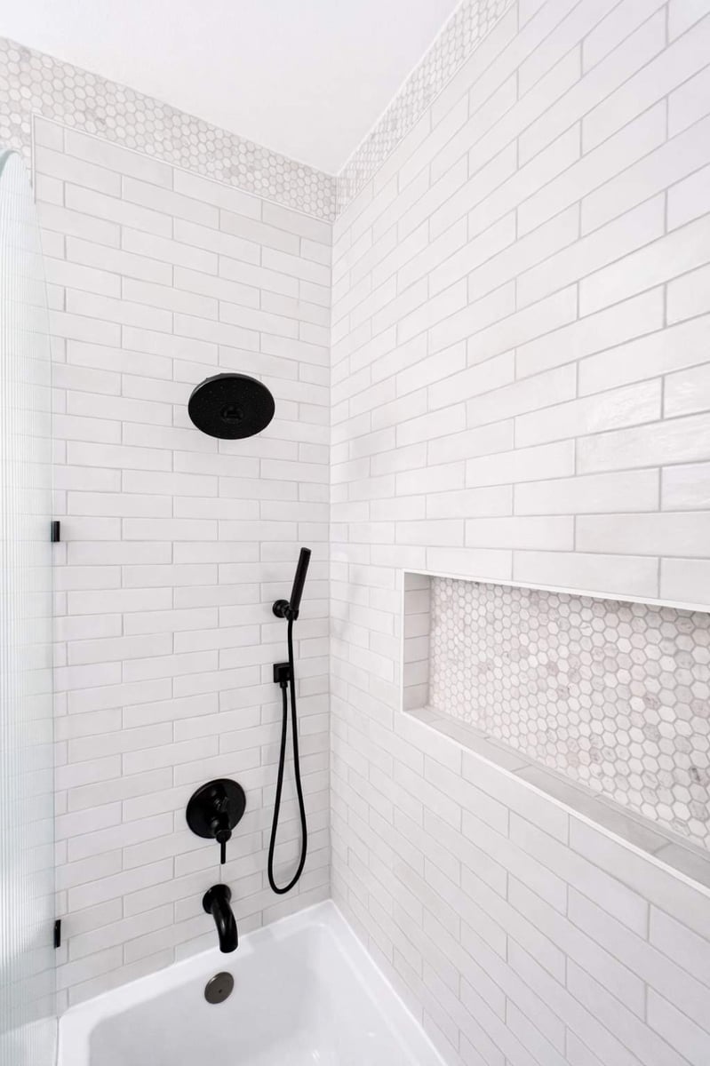 White subway tile tub surround with black rainfall head and mosaic niche