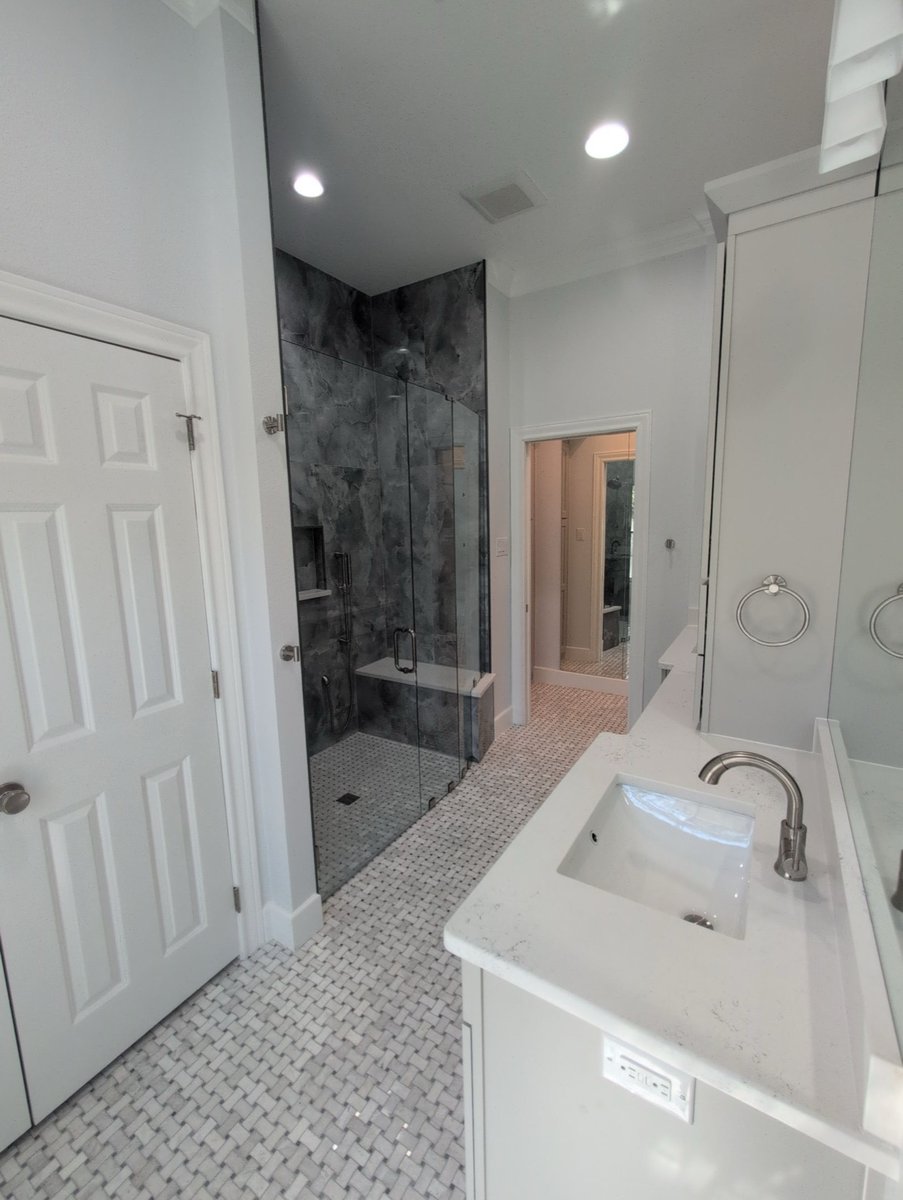 Long bathroom with gray stone shower, white sink, and basketweave floor