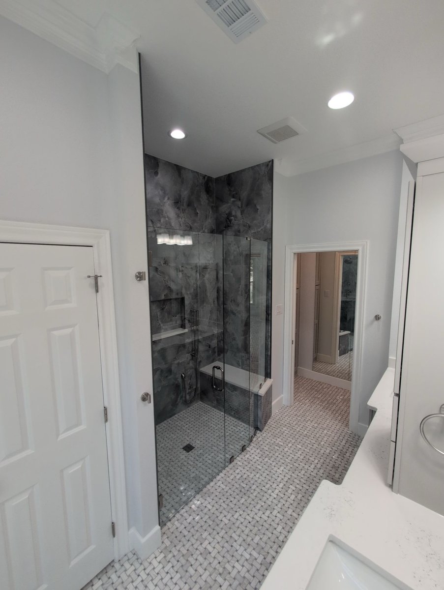 Glass shower in gray onyx-look stone with hallway view beyond