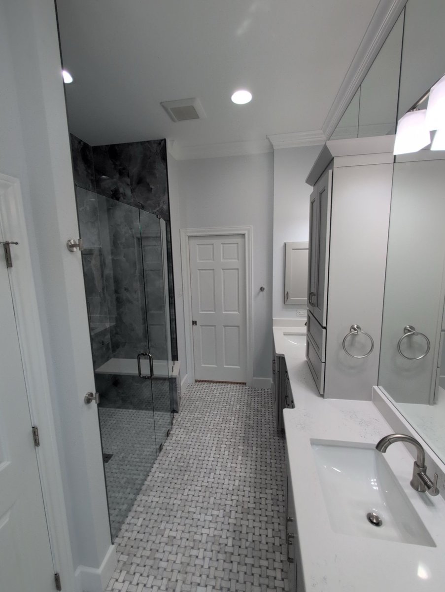 Narrow bath with frameless gray stone shower and gray double vanity