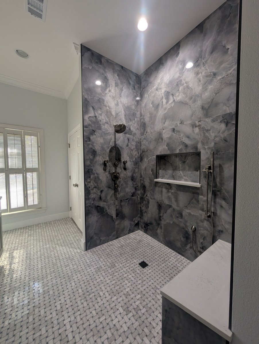 Walk-in shower clad in dramatic gray onyx-look tile with basketweave floor