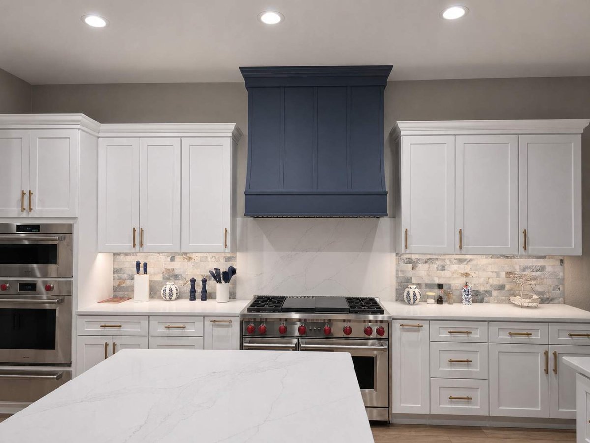 White kitchen centered on navy vent hood above a stainless range and stone backsplash