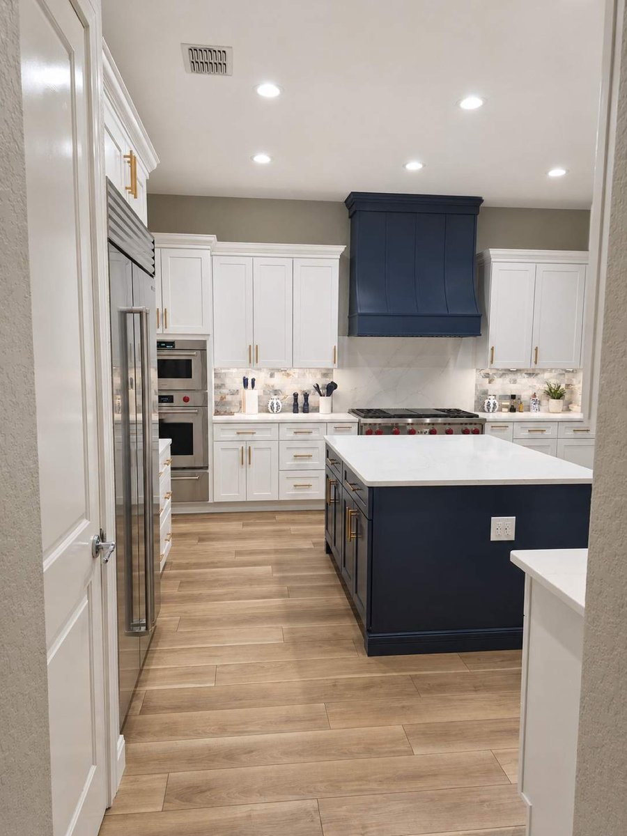 View into white kitchen with navy island and matching navy board vent hood