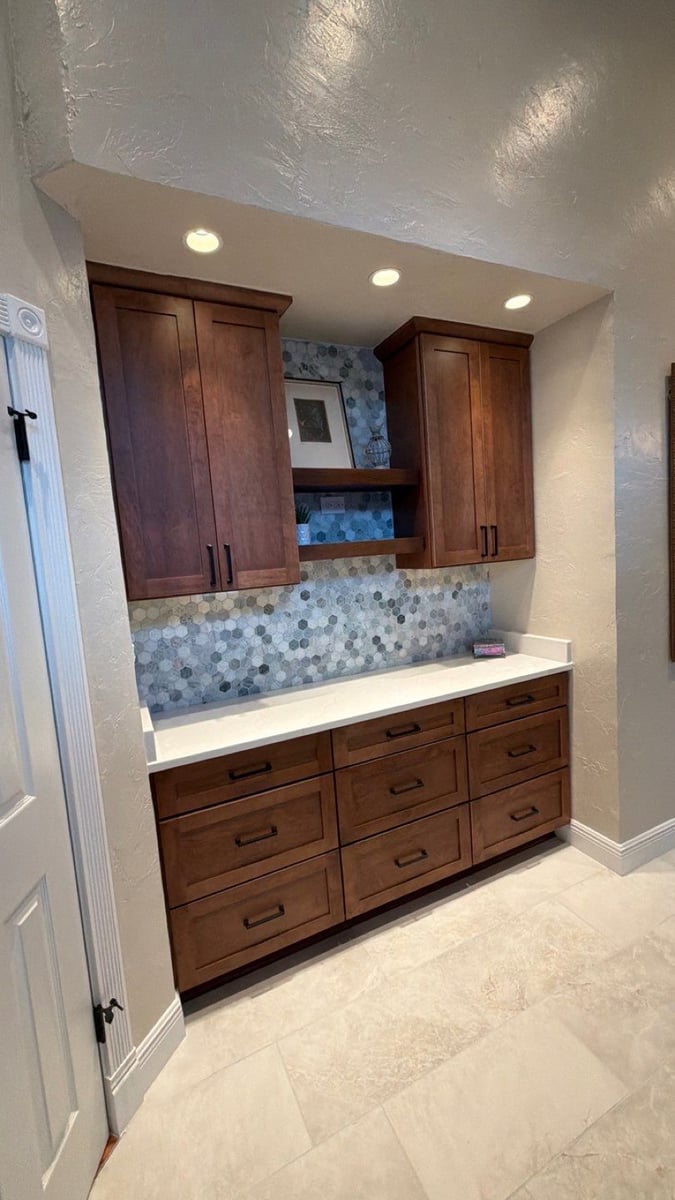 Dark wood vanity wall with blue hexagon tile backsplash, floating shelves, and white quartz top