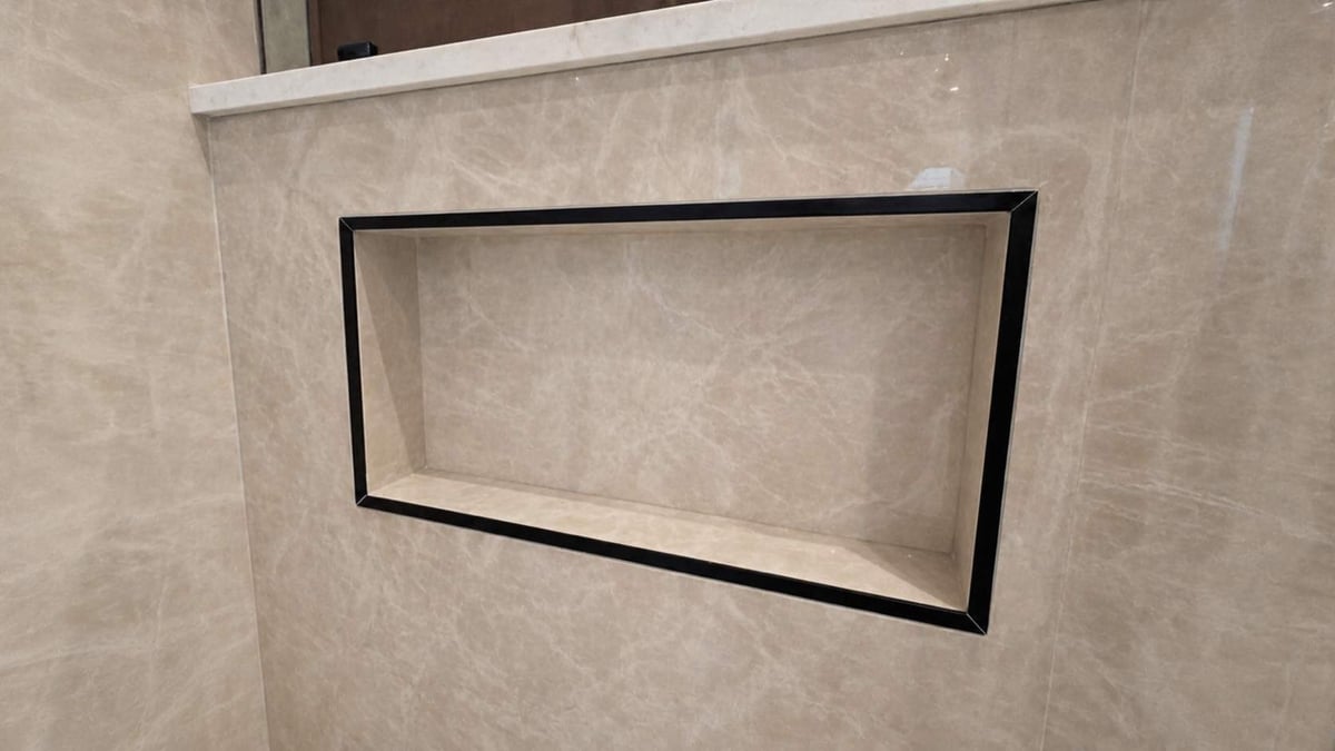 Recessed shower niche with black trim set in beige marble wall