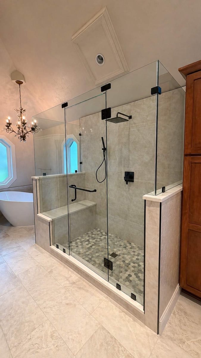 Frameless glass walk-in shower with bench and black fixtures under coffered ceiling