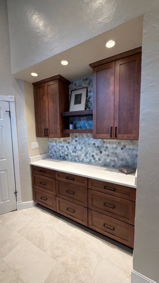 Wood cabinet wall with blue hexagon backsplash, floating shelves, and white counter