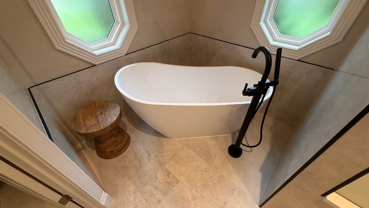 White freestanding slipper tub in corner with octagon windows and black floor faucet