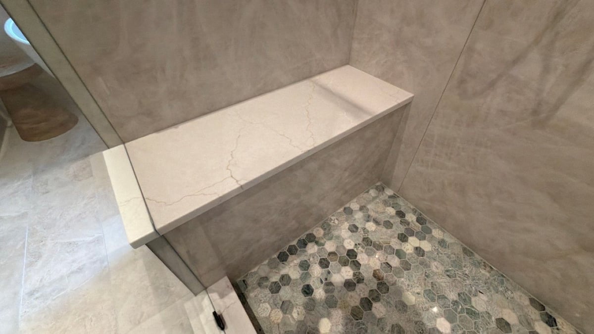 Quartz shower bench above green hexagon mosaic floor against gray marble walls