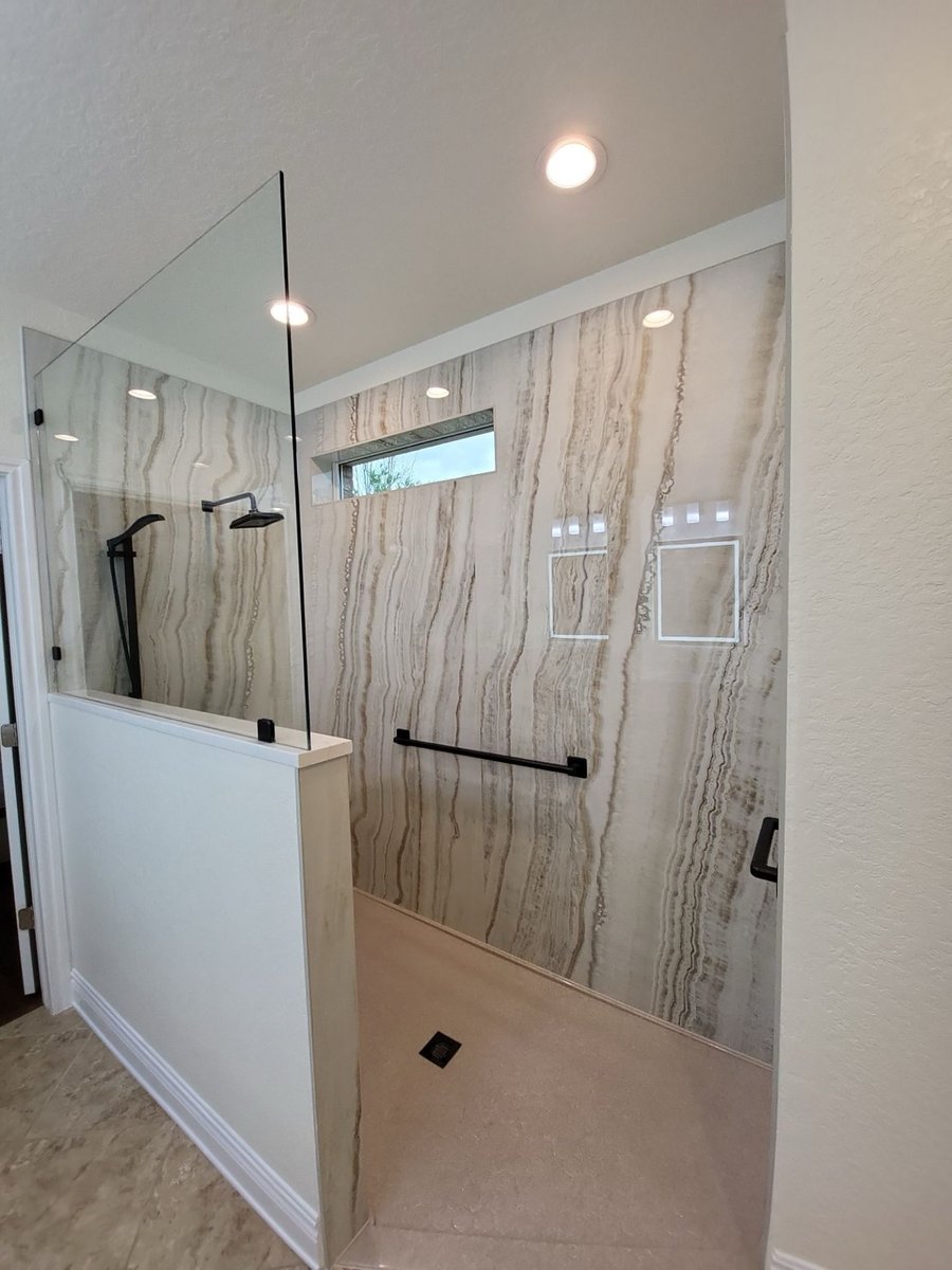 Curbless walk-in shower with veined stone walls, glass panel and black grab bar