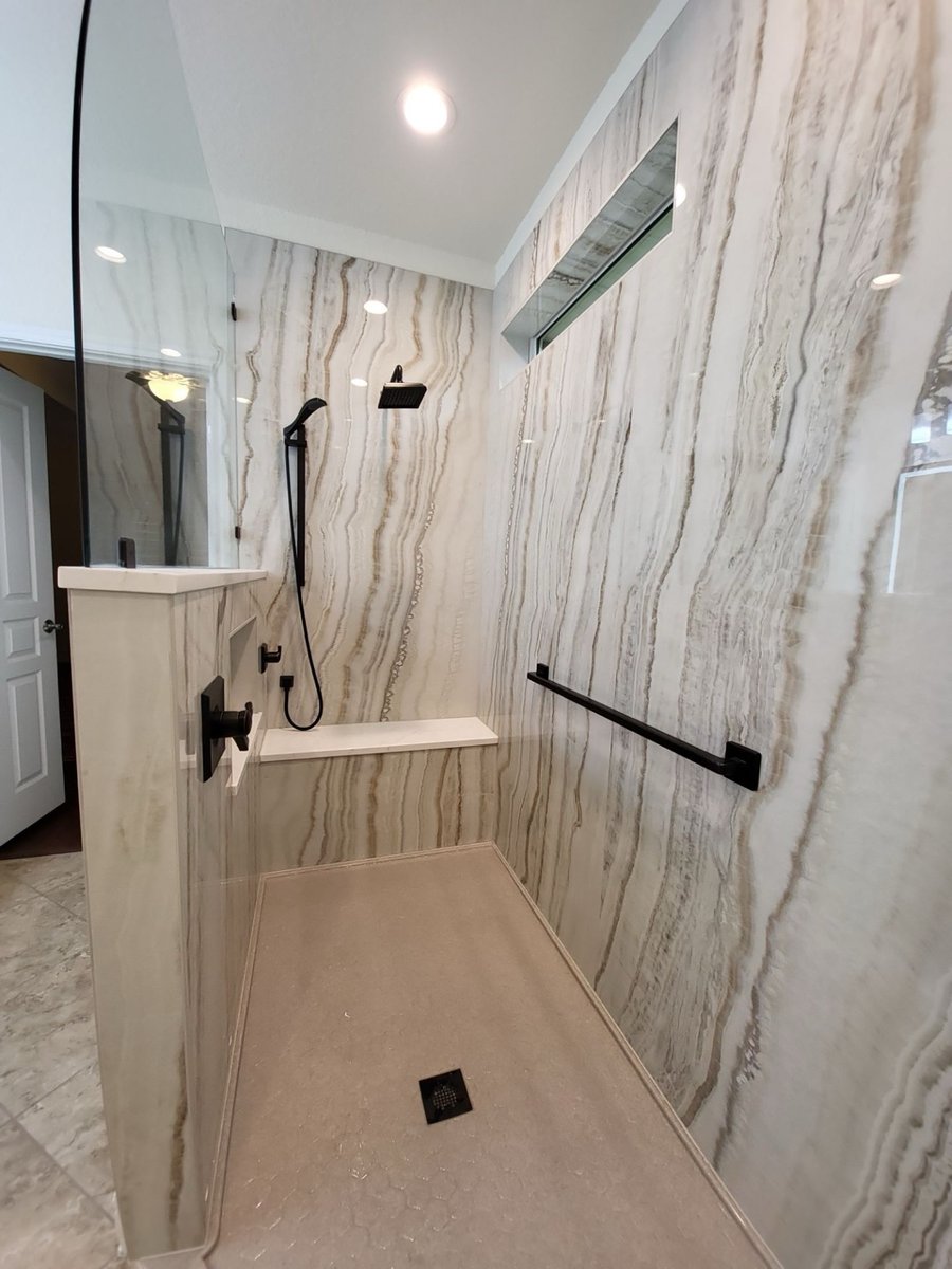 Roll-in shower with light veined walls, black fixtures, bench and floor drain