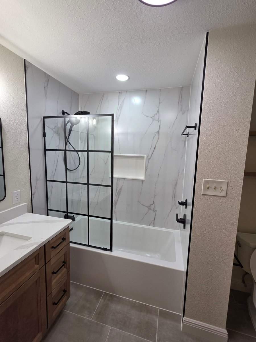 Bathtub-shower combo with white marble walls, black grid glass screen, and wood vanity