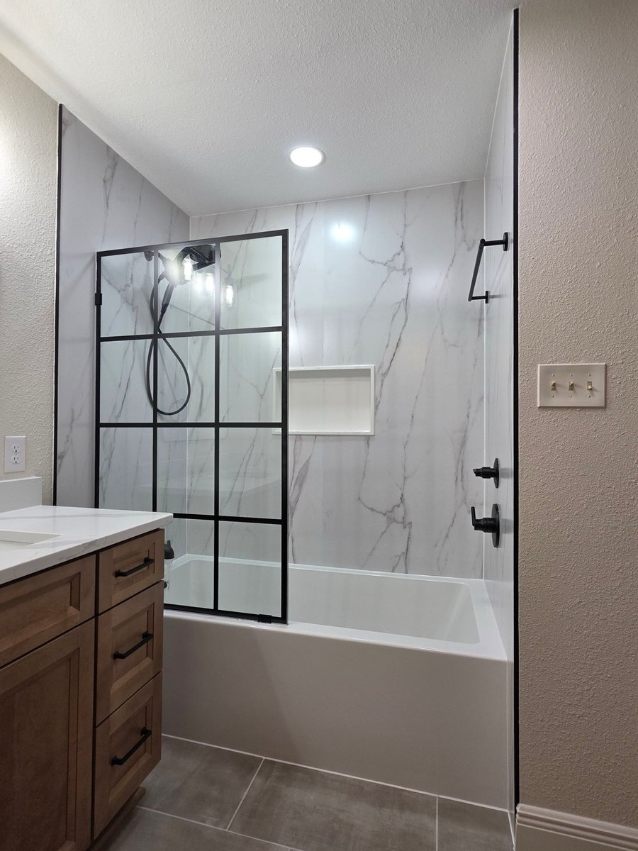 Marble-walled tub and shower with black grid glass partition and recessed niche
