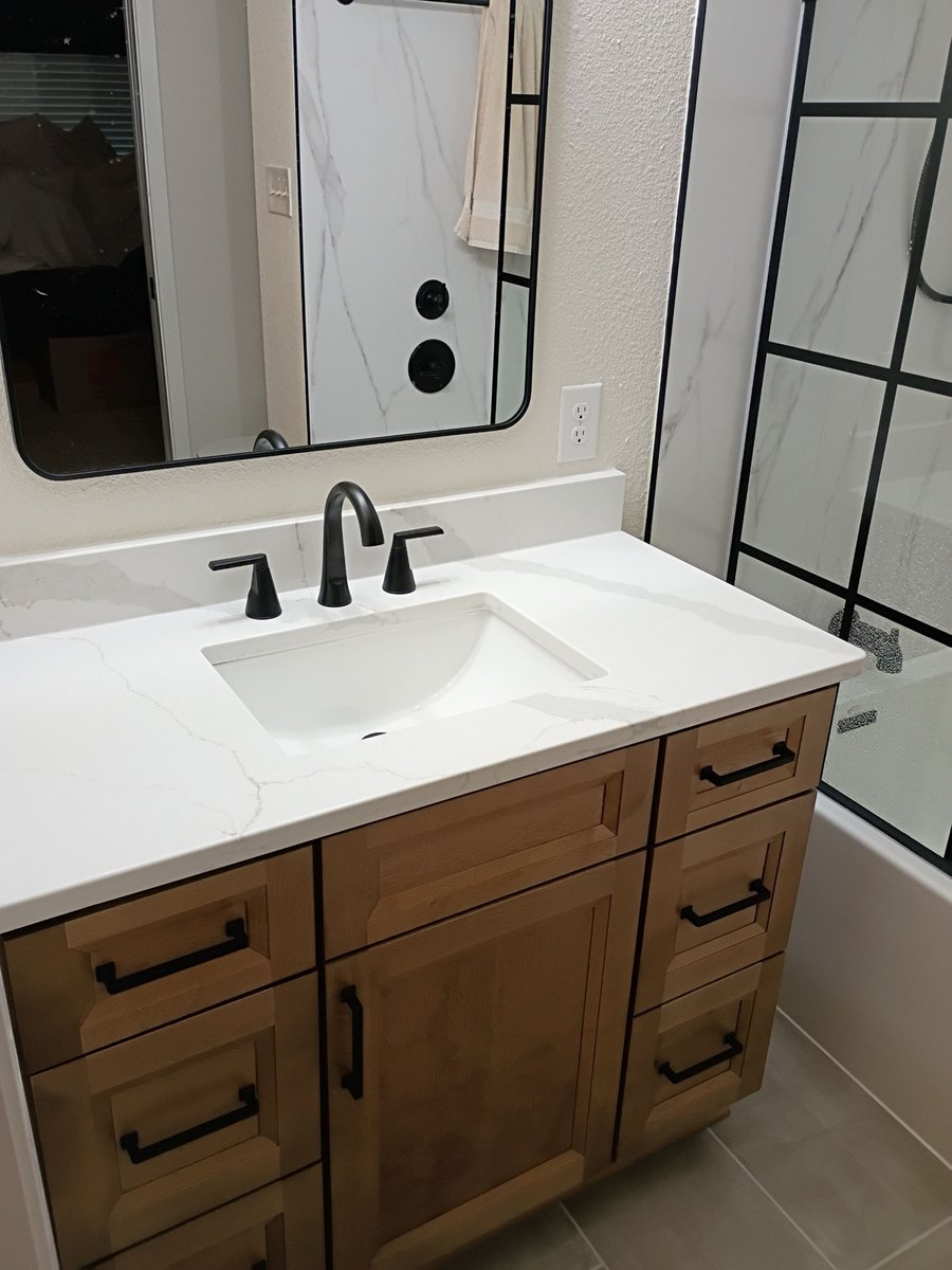 Close-up of white quartz vanity top with undermount sink and black widespread faucet